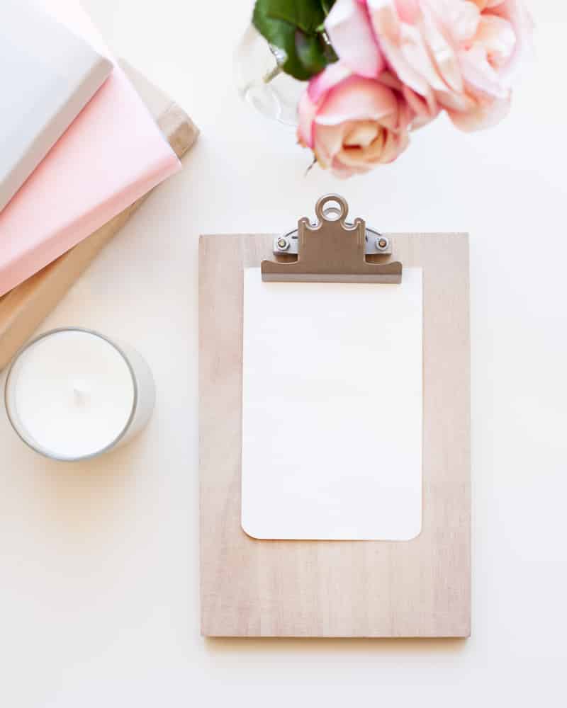 a clipboard, flower, candle and journals on a desk