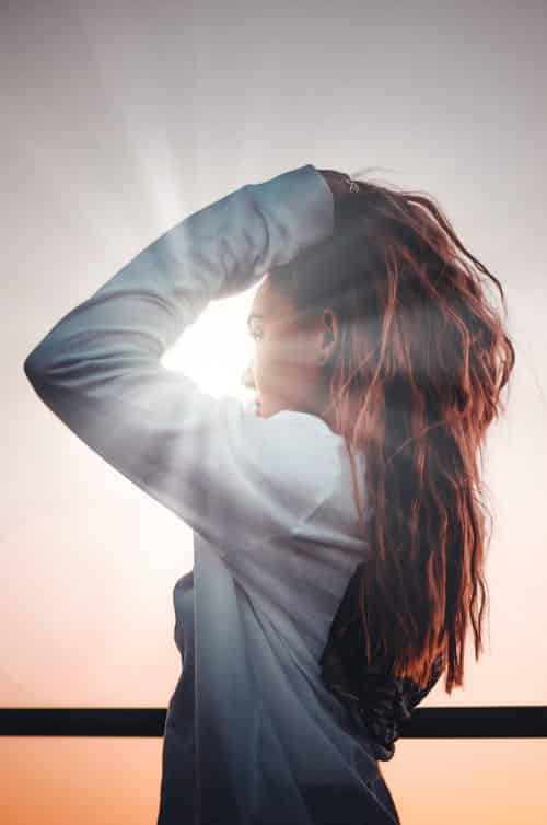 Woman with her hands in her hair, the sun is shining through the gap in her arms