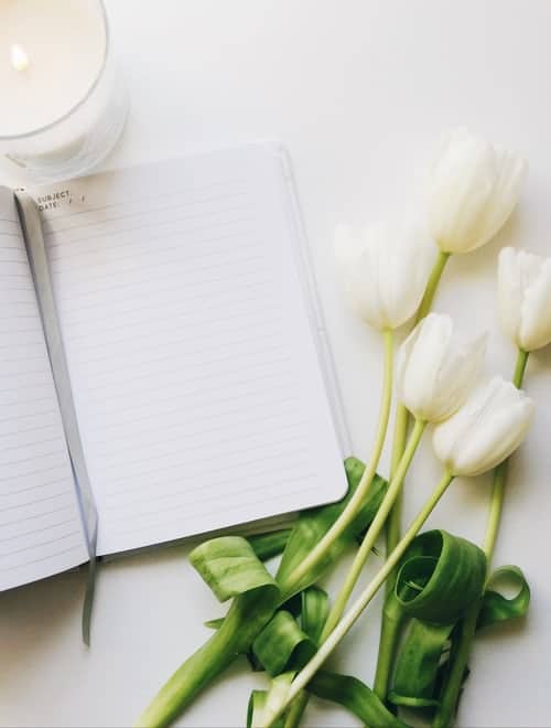 an open journal with white roses and a candle on a desk