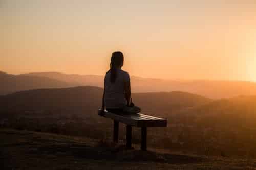 A woman sitting on a bench on a hilltop watching the sunset