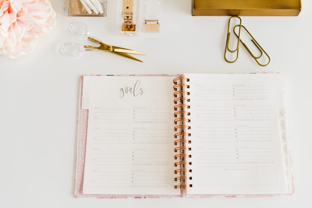 an open journal that says goals at the top laying open on a desk with stationary surrounding it