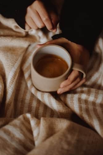 A person's hands holding a mug of coffee on top of a blanket