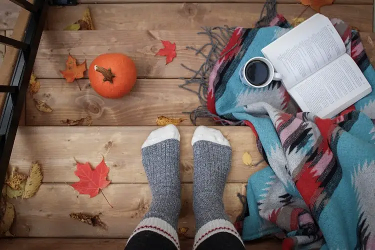 A person wearing socks; a pumpkin, open book, coffee and blanket on some steps
