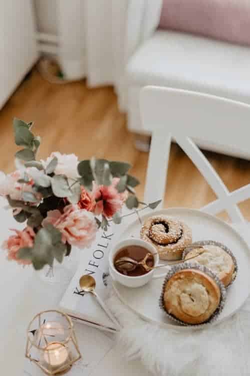 Pastries and tea on a plate next to some flowers and a candle