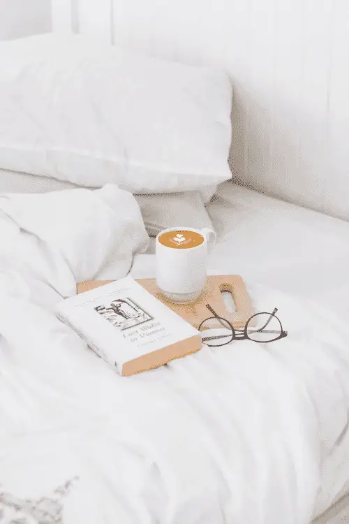 A coffee, reading glasses and book in an unmade bed