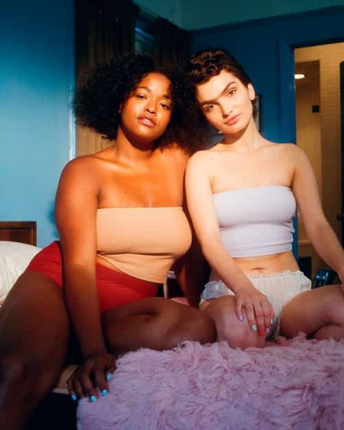 two women sitting on a bed together staring into the camera