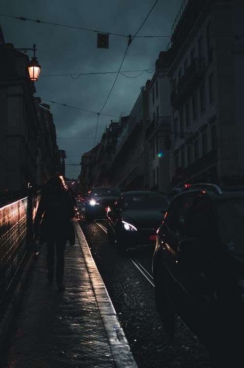 A person walking down a street at night with cars driving past