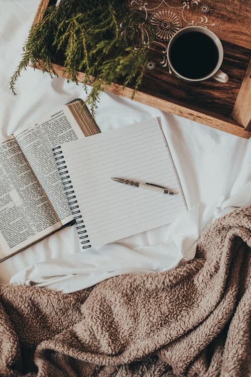 A notebook, book, cup and tray on a bed