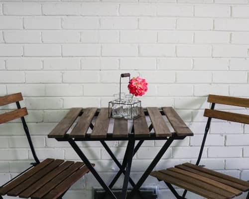 a wooden table with a flower in the middle and two empty chairs