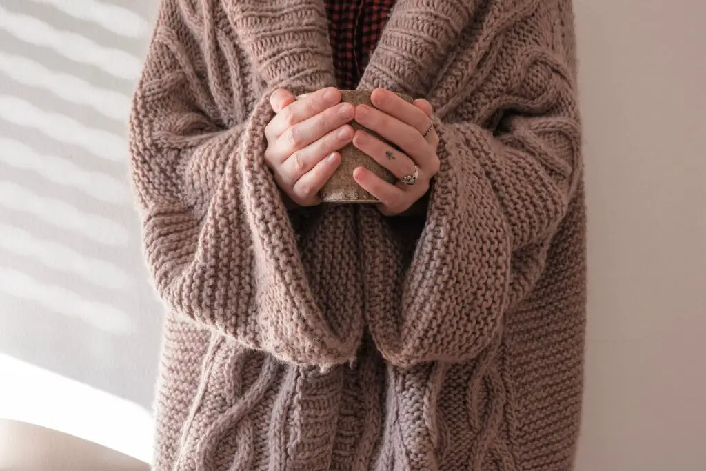 A person in a large cosy cardigan, cradling a mug of hot drink