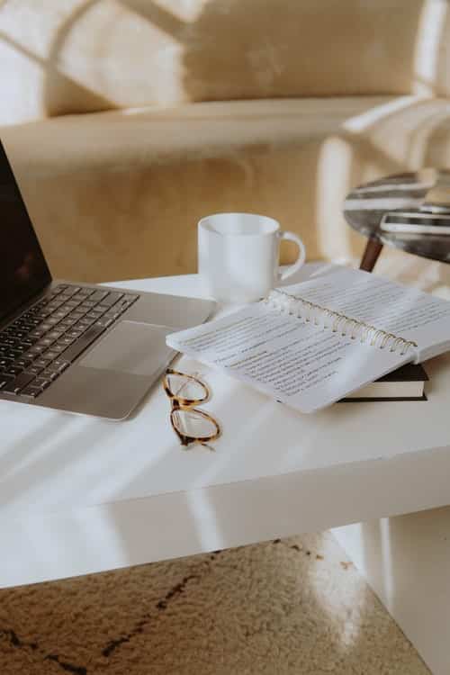 open journal, glasses, mug, and laptop on a table