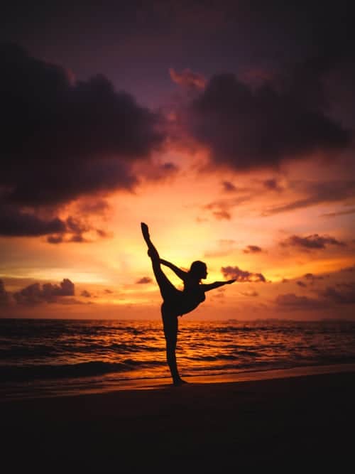 A woman doing yoga stretches on the beach at sunset