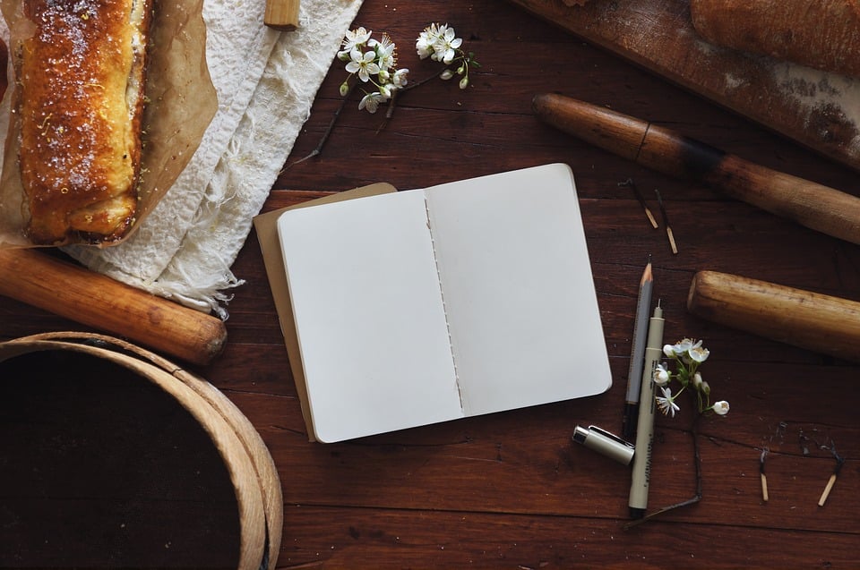 An blank open journal on a table with fresh bread and flowers
