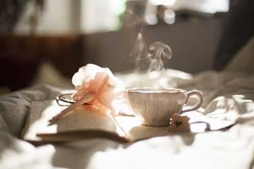 A steaming cup of tea on an open journal on a bed