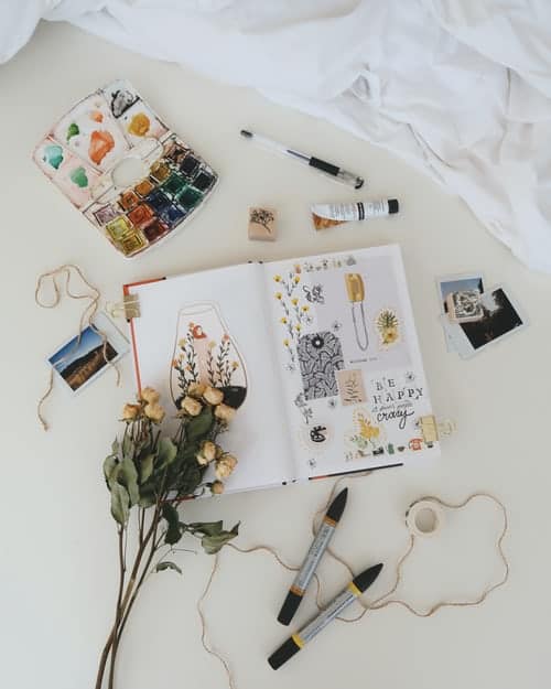 A bullet journal filled with doodles surrounded by art supplies