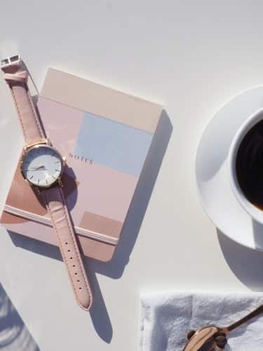 a notebook, watch and cup of coffee on a table