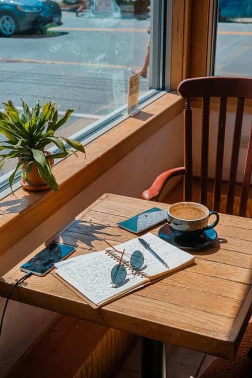 a coffee, open notepad, phone, and pen on a wooden table at a cafe