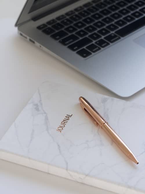 A journal, pen and laptop on a desk