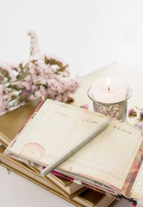 an open planner, flowers and a candle on a desk