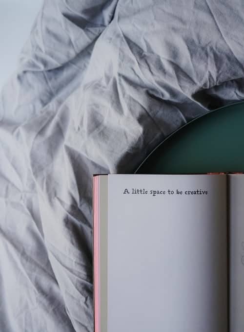 an open notebook on a bed; the notebook reads "a little space to be creative"
