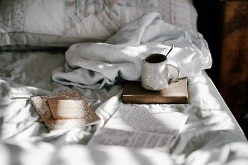 notebooks and a cup on an unmade bed