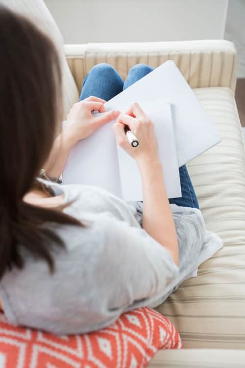 A woman sat on a sofa writing in her journal.