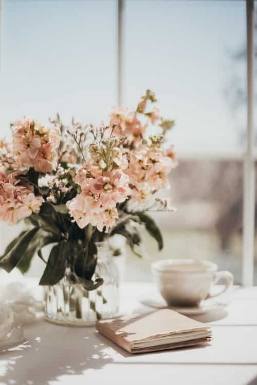 a vase of flowers, tea cup, and notebook on a table