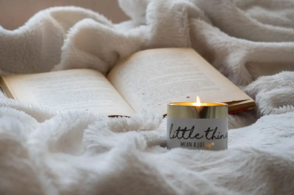 An open book and lit candle on a soft blanket