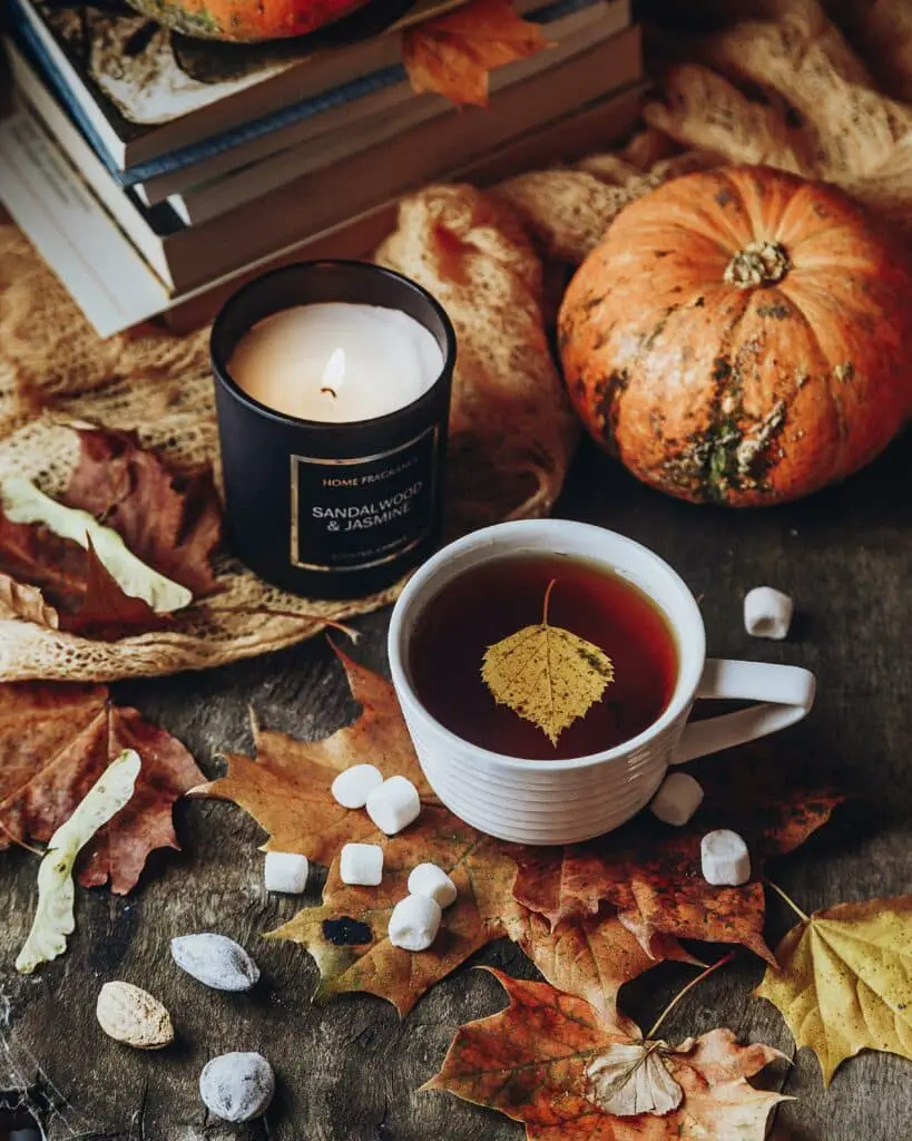 A candle, pumpkin, and tea on a table decorated with autumn leaves