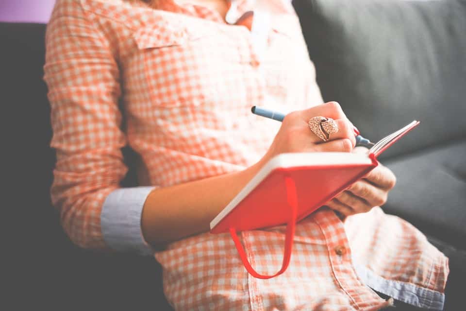 A woman sitting on a couch, writing in her journal