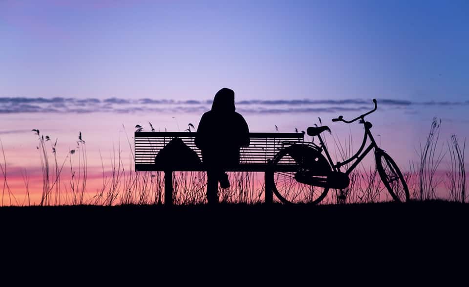 Silhouette of a person and their bicycle sitting on at sunseta bench