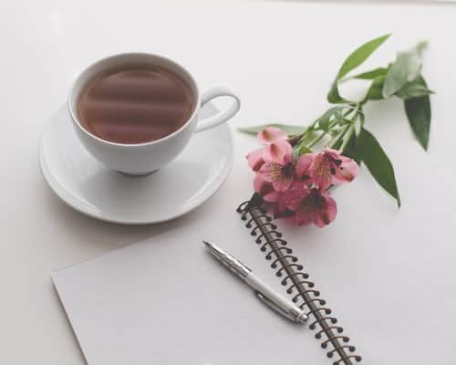 a cup of tea, flowers and notepad on a table