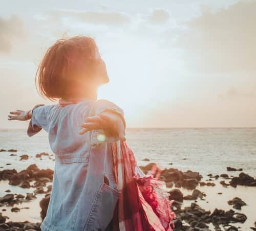 a woman with her arms outstretched on a beach looking out to sea