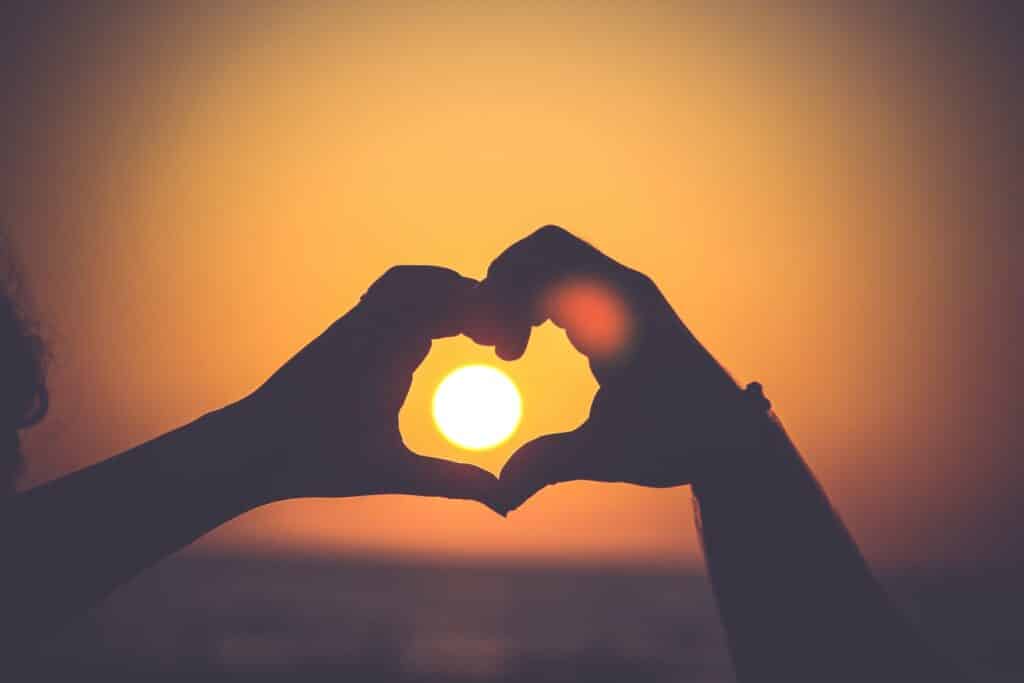 Two hands making a love heart shape in front of the sun