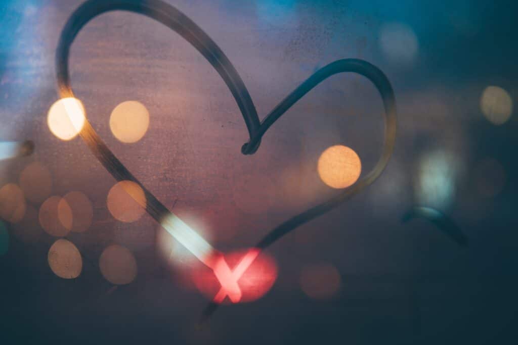 A love-heart drawn in a foggy window with street lights in the distance