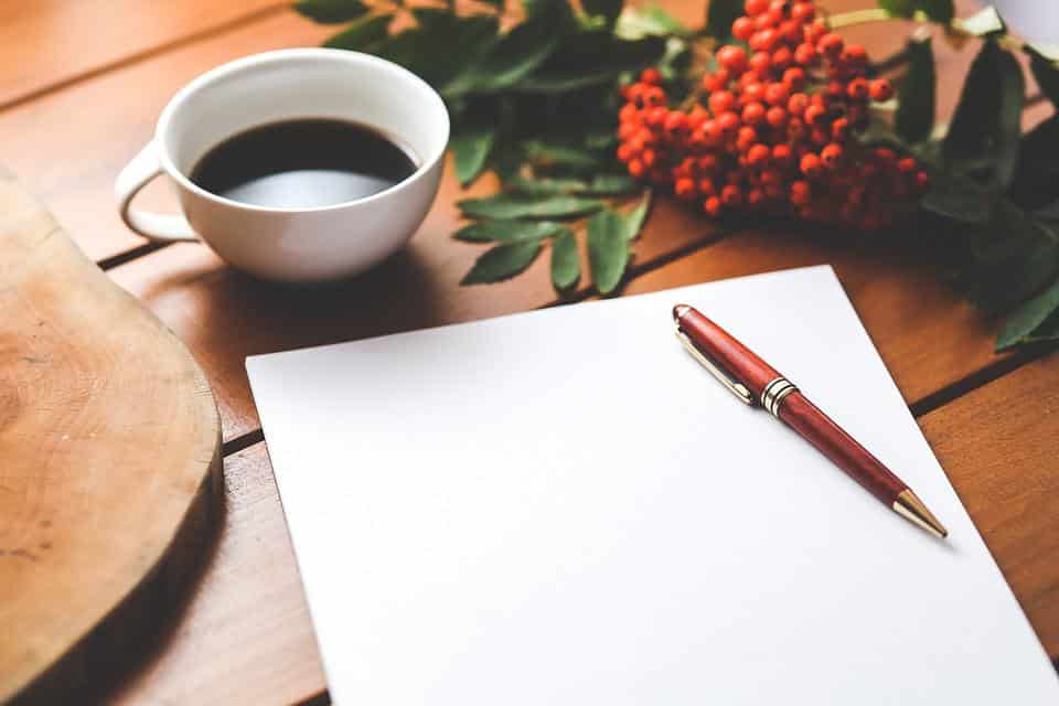 A journal, pen, black coffee and flowers on a wooden table