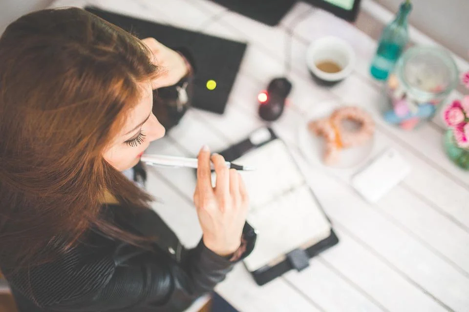 A woman sitting at a desk; in front of our is an open planner.