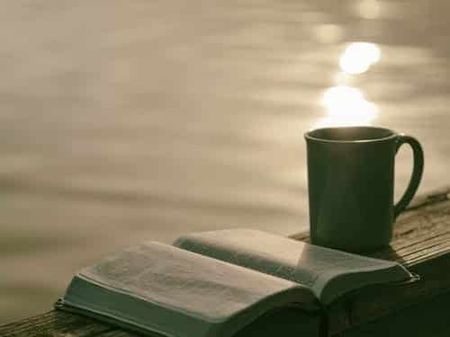 An open book and mug on a balcony overlooking the sea
