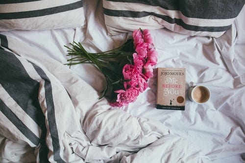 A bouquet of flowers, a book, and cup of coffee on an unmade bed