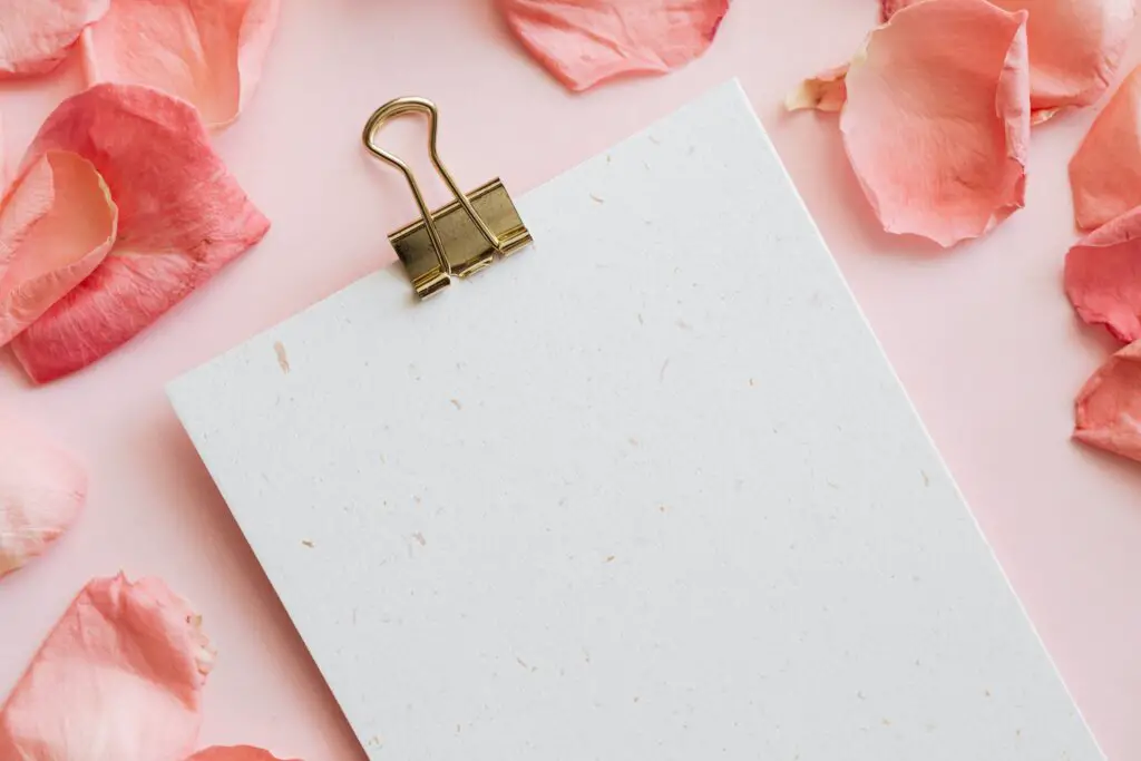 A clipboard sits on top of a pale pink desk surrounded by pink flower petals.