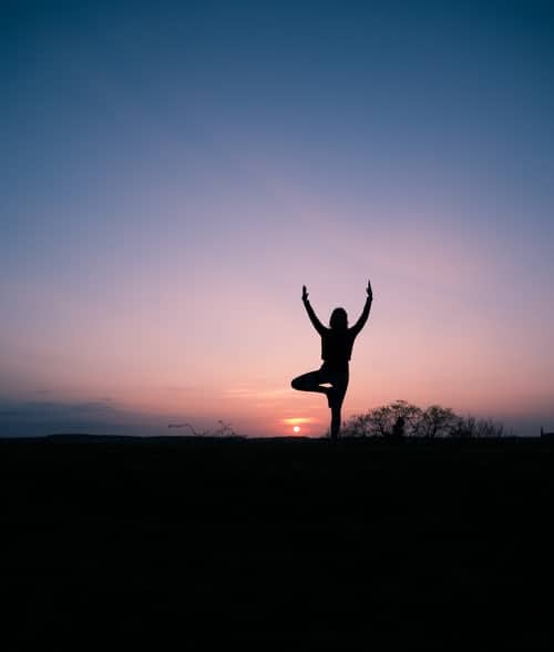 A person's silhouette doing yoga in a field