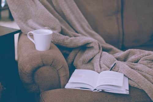 A mug, book and blanket on a sofa