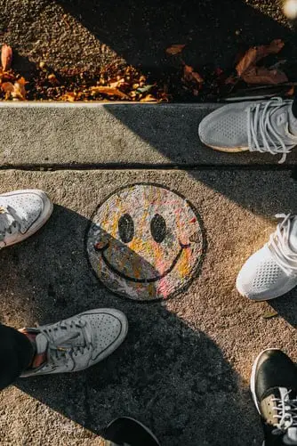 Two people's feet standing either side of a smiley face drawn on the pavement
