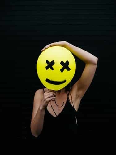 A person holding a balloon with a smiley face drawn on it in front of her own face