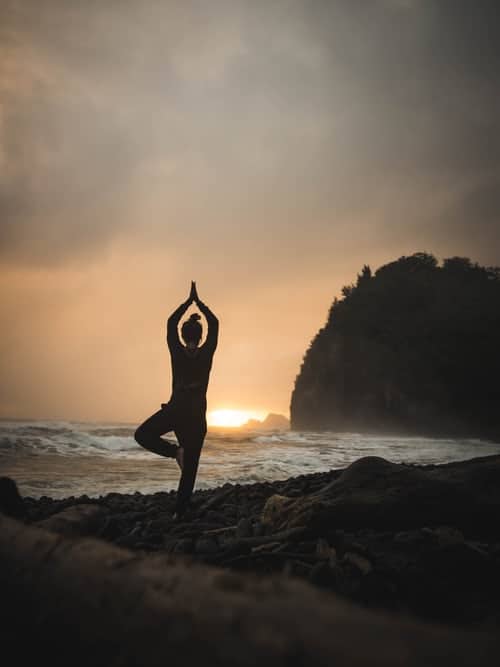 A woman practising yoga on a pebble beach at sunrise