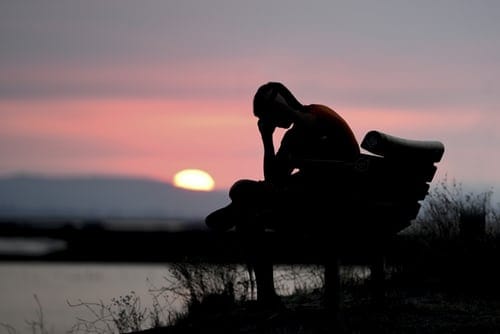 The silhouette of a person sitting on a bench next to a lake