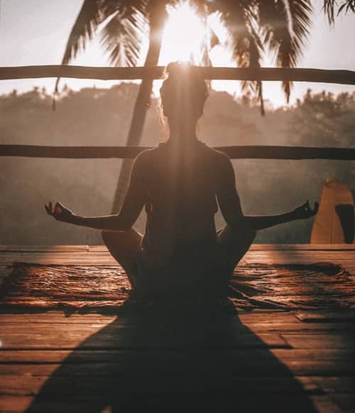 A woman meditating at sunrise on her balcony
