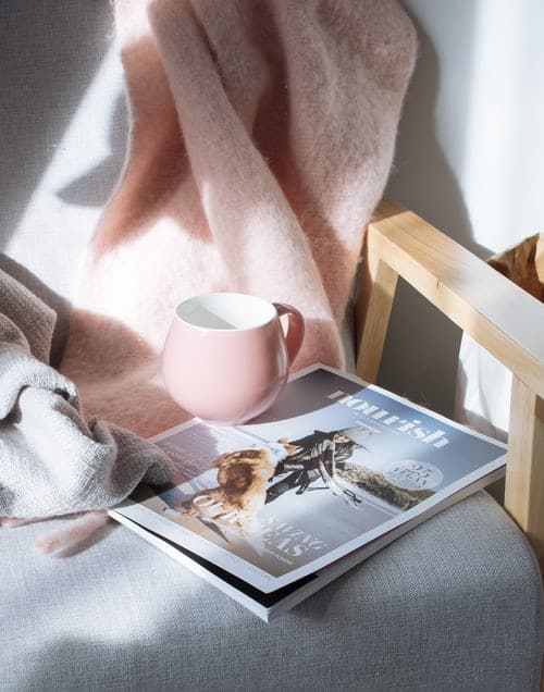 A chair with a magazine, cup and blanket on it