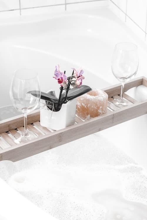 A bath tray with wine glasses, a candle and flower on it