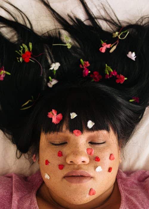 woman laying down with her eyes closed and flower petals in her hair